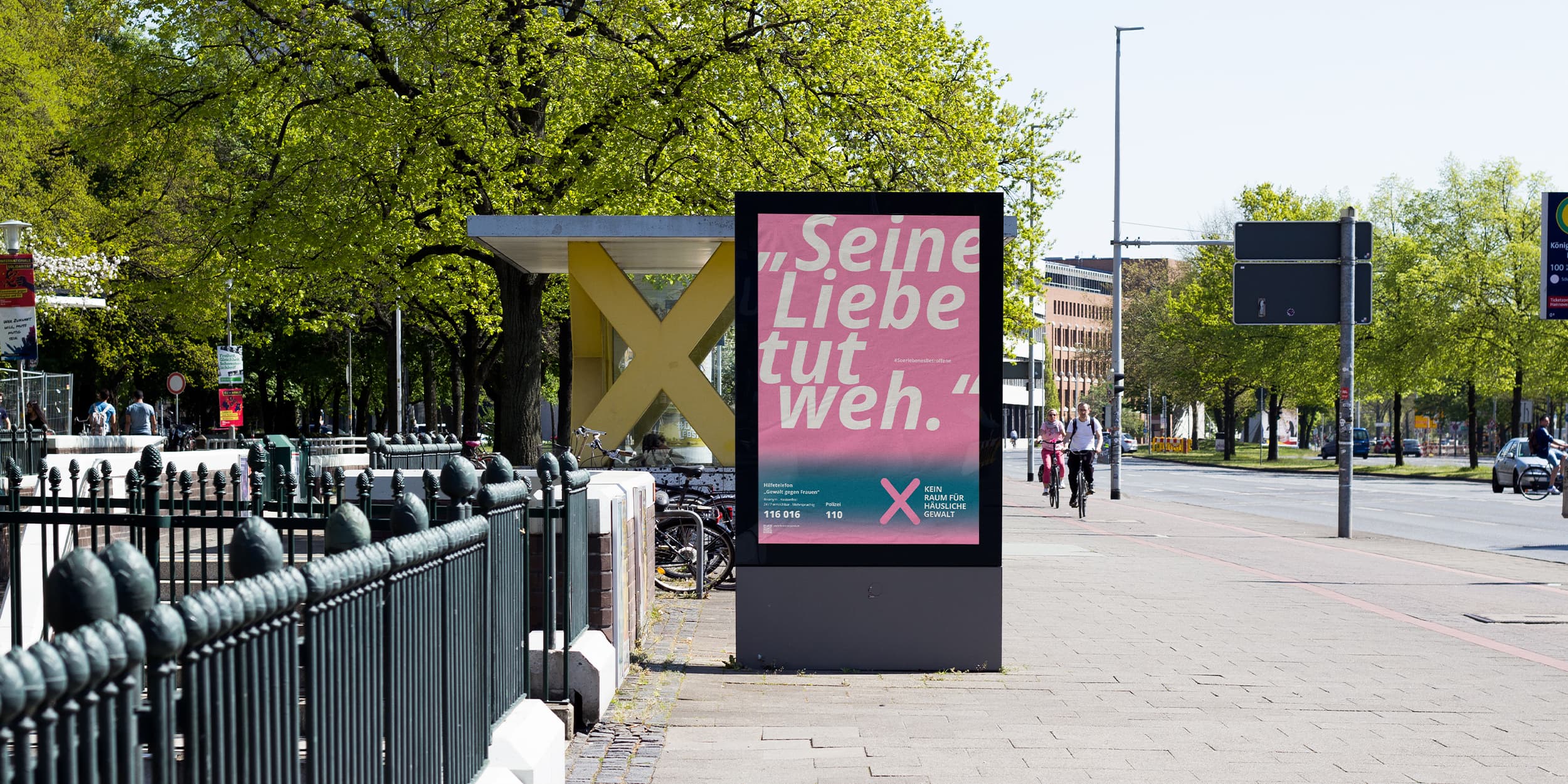 Plakat der Kampagne „Kein Raum für häusliche Gewalt“ mit dem Zitat „Seine Liebe tut weh“ und Hinweisen auf Hilfsangebote, platziert auf einer Werbefläche im öffentlichen Raum.